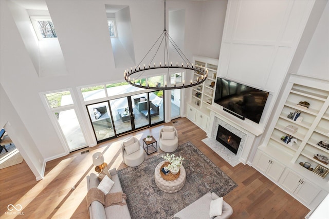 living room with a high end fireplace, hardwood / wood-style flooring, built in features, a towering ceiling, and a chandelier