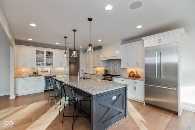 kitchen with sink, premium range hood, built in refrigerator, a kitchen island with sink, and range