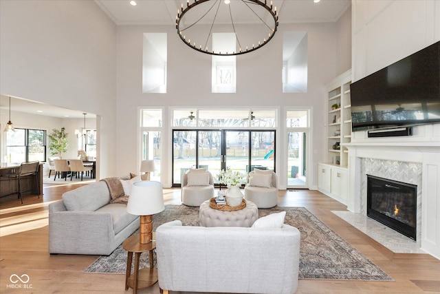 living room with a fireplace, a towering ceiling, light hardwood / wood-style floors, and built in features