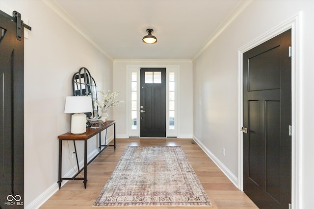 foyer entrance with a barn door, light wood-type flooring, and ornamental molding