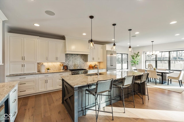 kitchen featuring white cabinets, sink, an island with sink, and hanging light fixtures