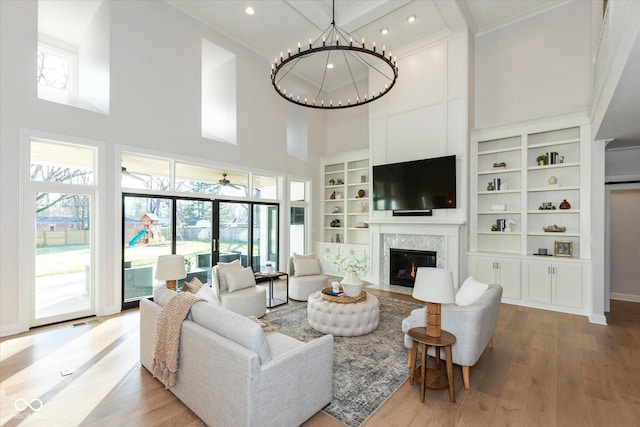 living room with a high end fireplace, ceiling fan with notable chandelier, built in shelves, a towering ceiling, and wood-type flooring