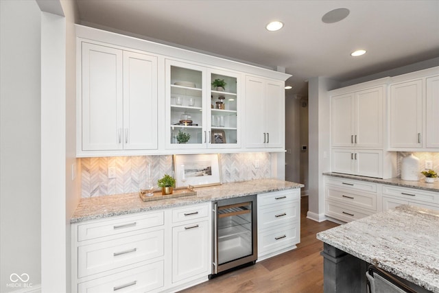 kitchen with hardwood / wood-style floors, backsplash, white cabinets, light stone countertops, and beverage cooler