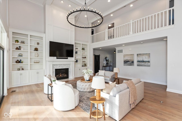 living room with built in shelves, light wood-type flooring, a high ceiling, and a chandelier