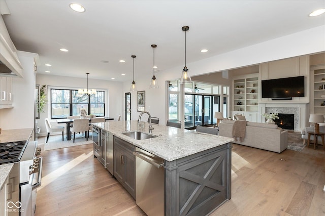 kitchen with light stone countertops, appliances with stainless steel finishes, sink, pendant lighting, and an island with sink