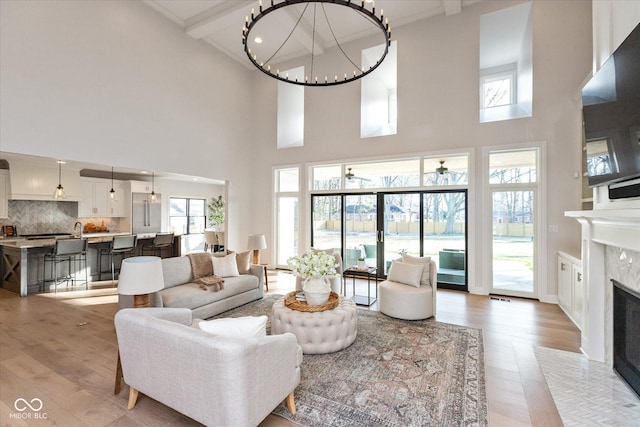 living room featuring a high end fireplace, beam ceiling, a towering ceiling, and light hardwood / wood-style flooring