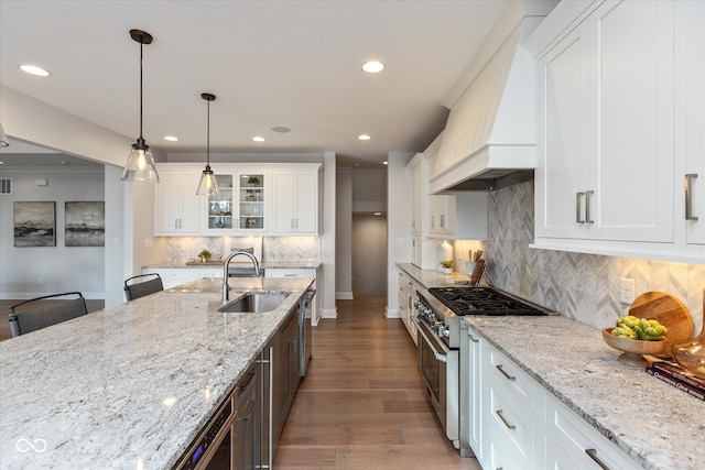 kitchen featuring high end stove, sink, white cabinets, and custom range hood