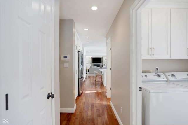 clothes washing area with cabinets, wood-type flooring, and washer and clothes dryer