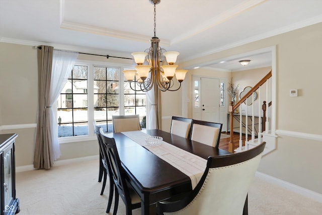 carpeted dining space with ornamental molding, a raised ceiling, and a chandelier