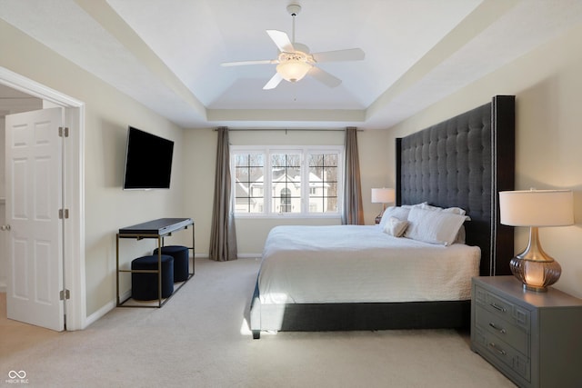 bedroom with ceiling fan, light carpet, and a tray ceiling