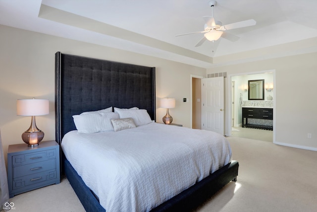 carpeted bedroom with ceiling fan, ensuite bathroom, and a tray ceiling