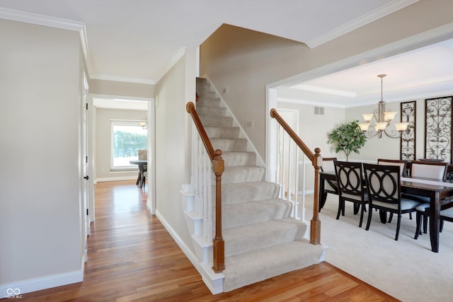 staircase featuring an inviting chandelier, ornamental molding, and hardwood / wood-style floors