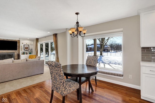 dining room with a brick fireplace, a notable chandelier, and hardwood / wood-style floors