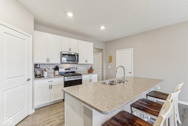 kitchen with sink, a breakfast bar area, appliances with stainless steel finishes, a kitchen island with sink, and white cabinets