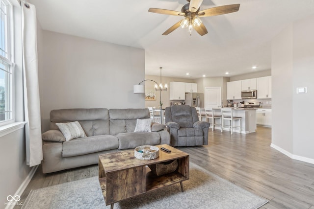 living room featuring ceiling fan with notable chandelier and light wood-type flooring