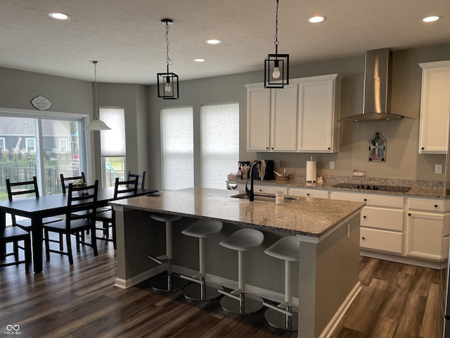 kitchen with black electric stovetop, wall chimney exhaust hood, a kitchen island with sink, sink, and white cabinets