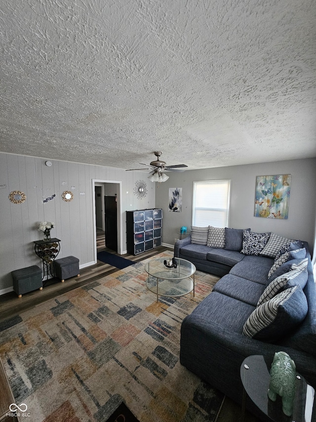 living room with wood walls, ceiling fan, and dark wood-type flooring