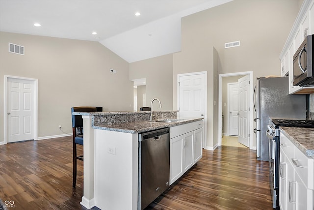 kitchen featuring stainless steel appliances, a kitchen island with sink, stone counters, white cabinets, and a breakfast bar area