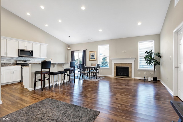 living room featuring a tiled fireplace, dark hardwood / wood-style flooring, and high vaulted ceiling