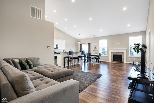 living room featuring dark hardwood / wood-style floors, high vaulted ceiling, and a tiled fireplace