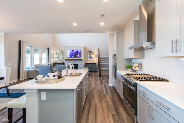 kitchen with appliances with stainless steel finishes, wall chimney exhaust hood, a breakfast bar, sink, and a center island with sink