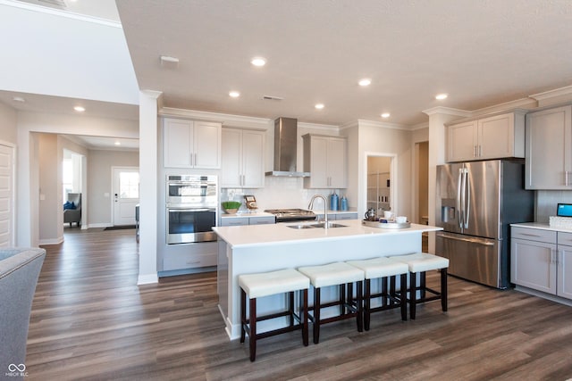 kitchen with stainless steel appliances, gray cabinets, a kitchen island with sink, and wall chimney range hood