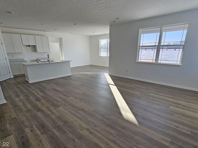 kitchen with a textured ceiling, a center island with sink, white cabinetry, and dark wood-type flooring