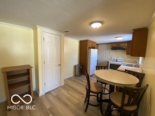 kitchen featuring light wood-type flooring, ornamental molding, a textured ceiling, white appliances, and sink