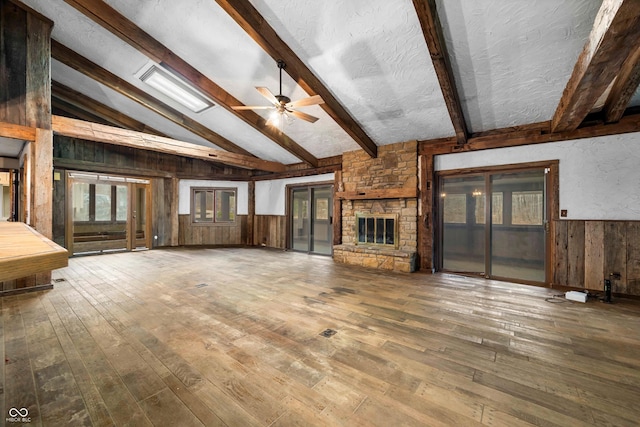 unfurnished living room with a fireplace, hardwood / wood-style floors, lofted ceiling with beams, and ceiling fan