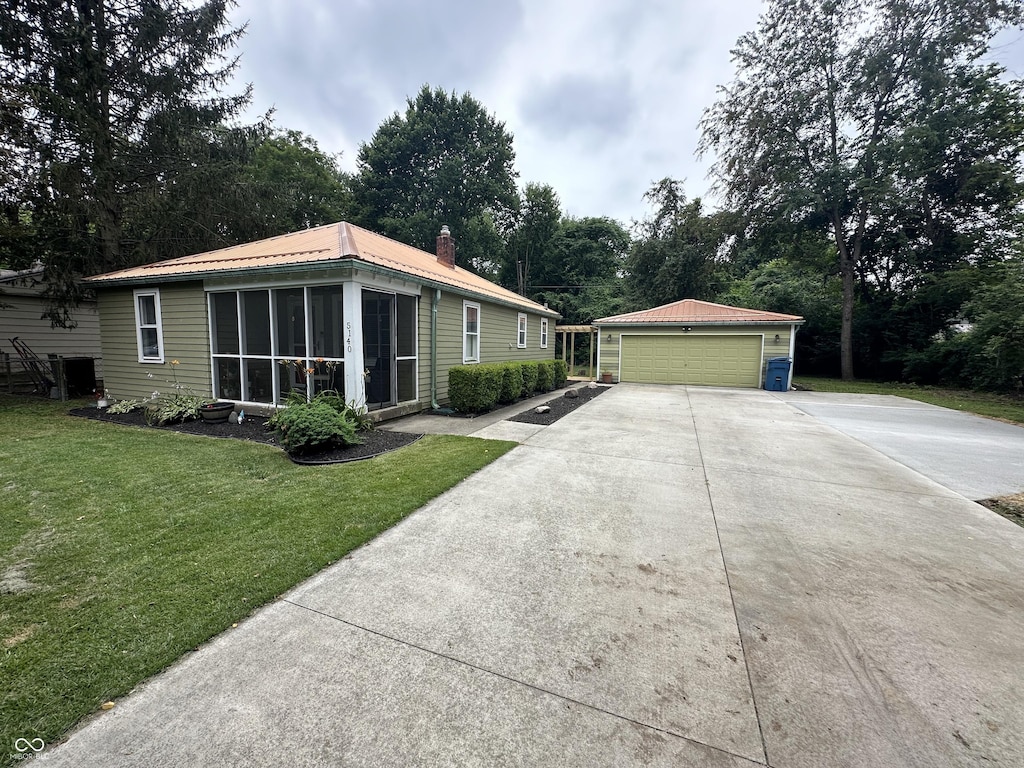 view of front of property featuring a sunroom, a garage, an outbuilding, and a front lawn