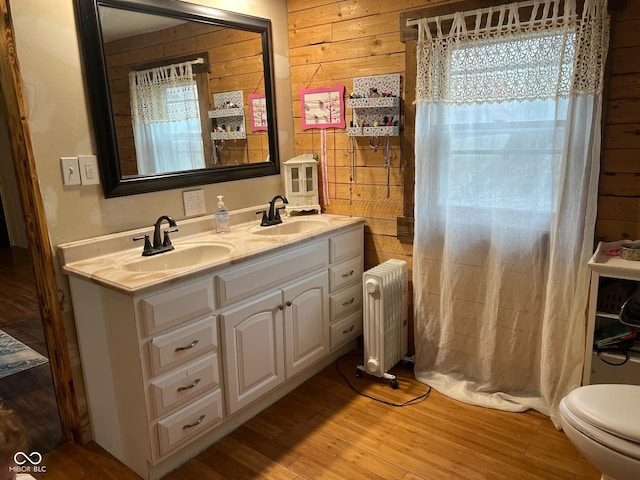 bathroom with radiator, wood walls, hardwood / wood-style floors, toilet, and vanity