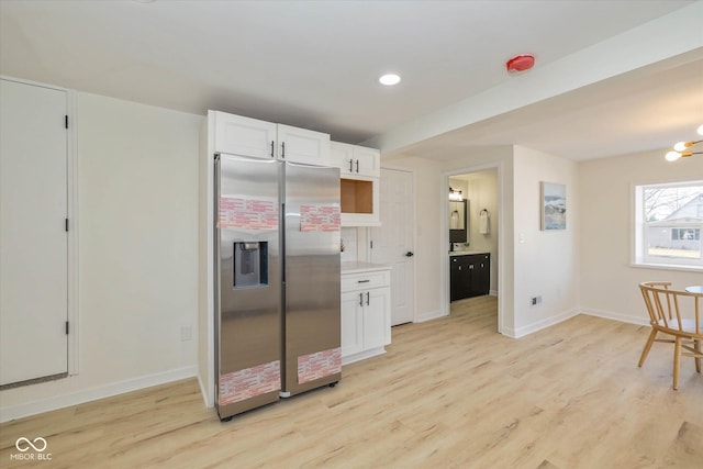 kitchen with stainless steel refrigerator with ice dispenser, a notable chandelier, light hardwood / wood-style floors, and white cabinets