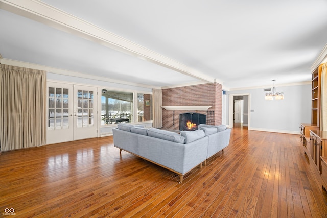 living room with an inviting chandelier, french doors, a brick fireplace, hardwood / wood-style flooring, and ornamental molding