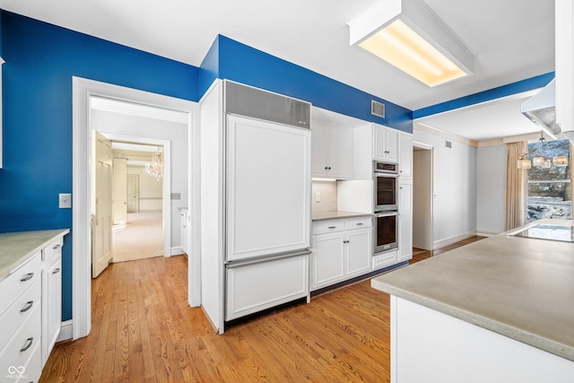 kitchen featuring white cabinets, paneled built in fridge, stainless steel double oven, and light hardwood / wood-style floors