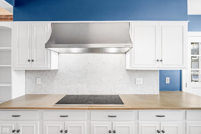 kitchen with white cabinets, black electric stovetop, and wall chimney range hood