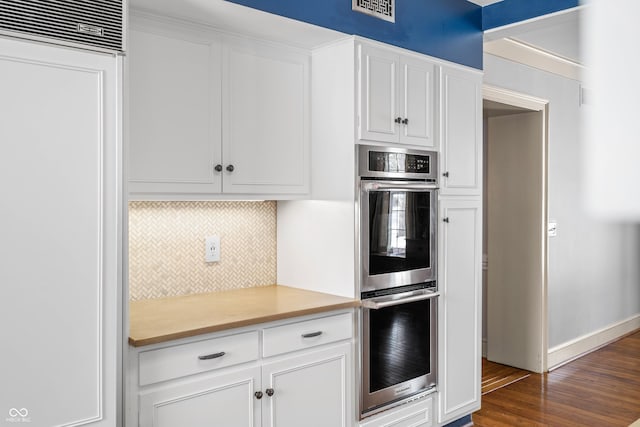 kitchen featuring white cabinetry, stainless steel double oven, dark wood-type flooring, and tasteful backsplash