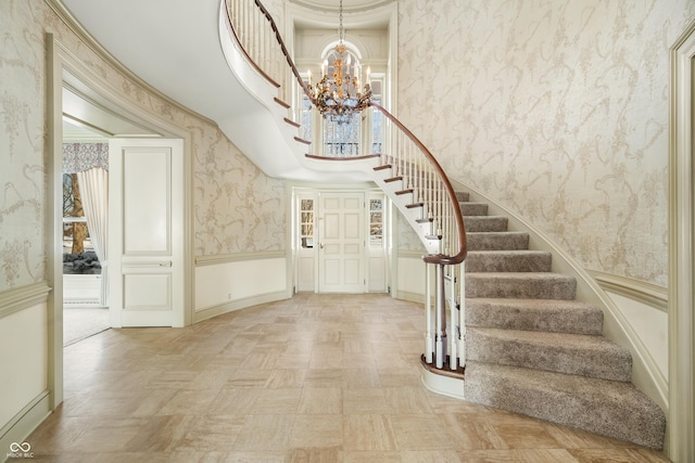 entrance foyer with light parquet flooring, a towering ceiling, ornamental molding, and a notable chandelier