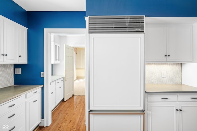 kitchen with white cabinets, paneled fridge, light wood-type flooring, and tasteful backsplash