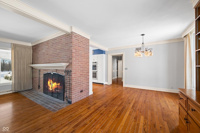 unfurnished living room featuring hardwood / wood-style floors, ornamental molding, a chandelier, and a brick fireplace