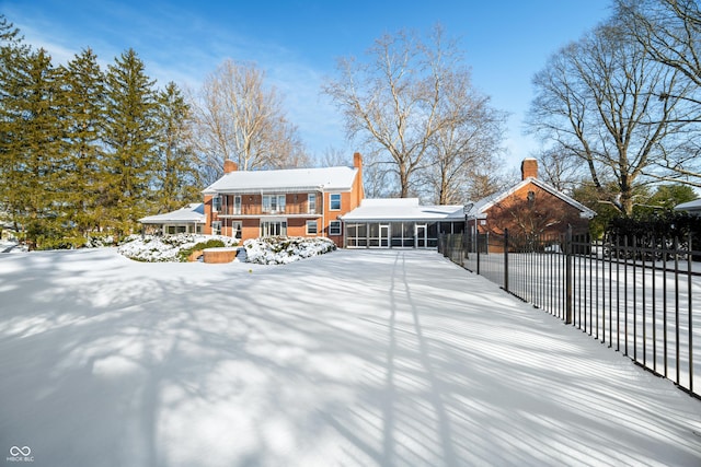 snow covered rear of property with a sunroom