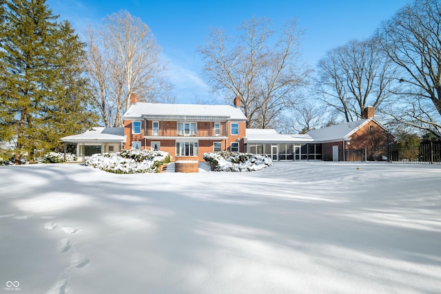 snow covered back of property featuring a sunroom