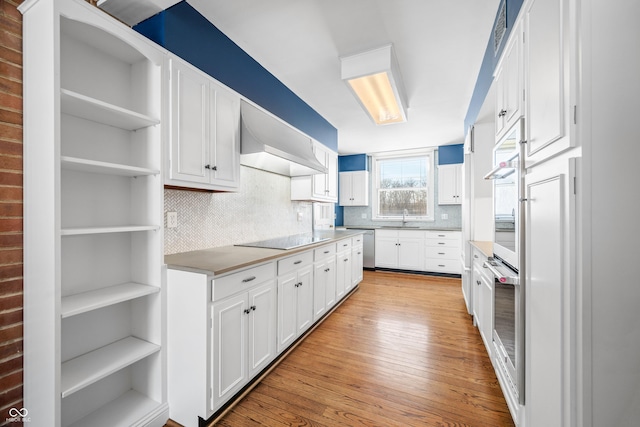 kitchen with appliances with stainless steel finishes, wall chimney exhaust hood, sink, light hardwood / wood-style flooring, and white cabinetry