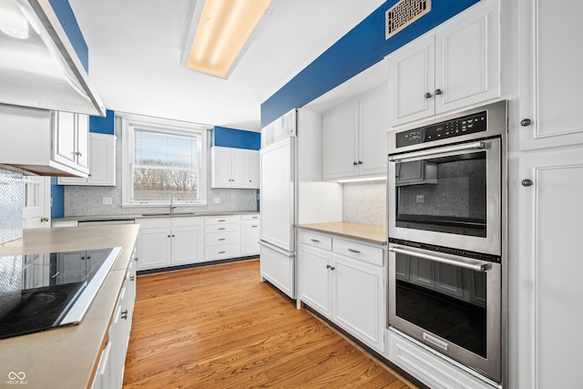 kitchen featuring double oven, electric stovetop, exhaust hood, light hardwood / wood-style flooring, and white cabinets