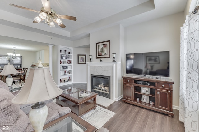 living room featuring built in shelves, ornate columns, a fireplace, and a tray ceiling