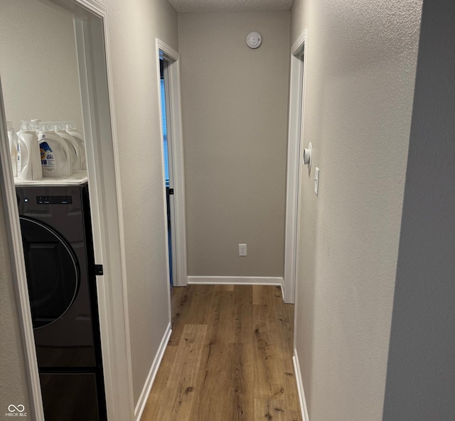 hall with washer / dryer, light hardwood / wood-style flooring, and a textured ceiling