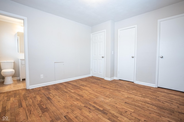 unfurnished bedroom featuring hardwood / wood-style floors, connected bathroom, and two closets