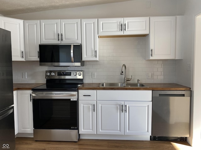 kitchen featuring wooden counters, stainless steel appliances, vaulted ceiling, sink, and white cabinets