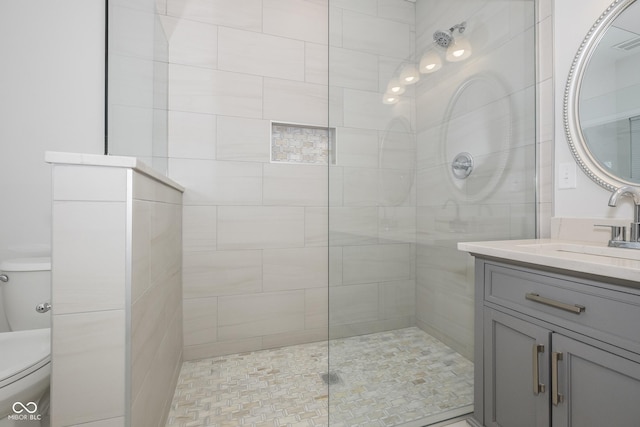 bathroom with tiled shower, vanity, and toilet