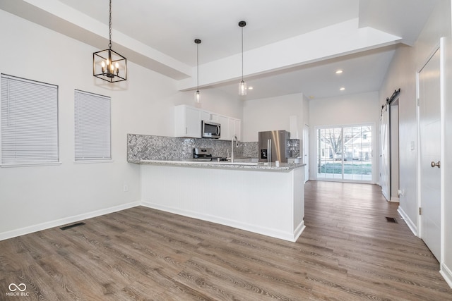 kitchen with kitchen peninsula, stainless steel appliances, a barn door, white cabinetry, and hanging light fixtures