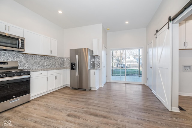 kitchen featuring a barn door, light hardwood / wood-style flooring, white cabinets, and stainless steel appliances